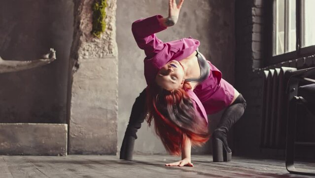 Slowmo of eccentric red haired girl in hot pink suit and high boots dancing vogue expressively on floor in authentic loft style studio