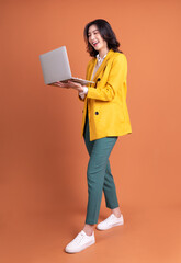 Full length photo of young Asian woman using laptop on background