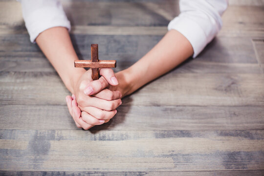 Christian woman doing praying hands and holding wooden cross on wood table. Concept for religious ,faith, spiritual ,Peace, hope 