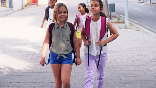 Two friendly preteen girls with backpacks talking while walking along city street on sunny summer day. High quality 4k footage