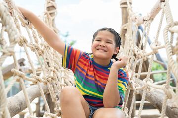 Happy Asian child girl playing on rope ladder at the playground on summer day. Smiling kid girl...