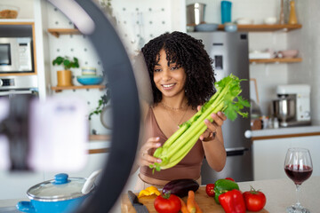 Young woman videoblogger cooking at the kitchen and filming. African American woman vlogger baking and recording video for food channel.