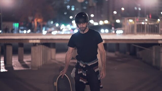 Skate model posing for a picture holding skateboard in the night city - lights in the background