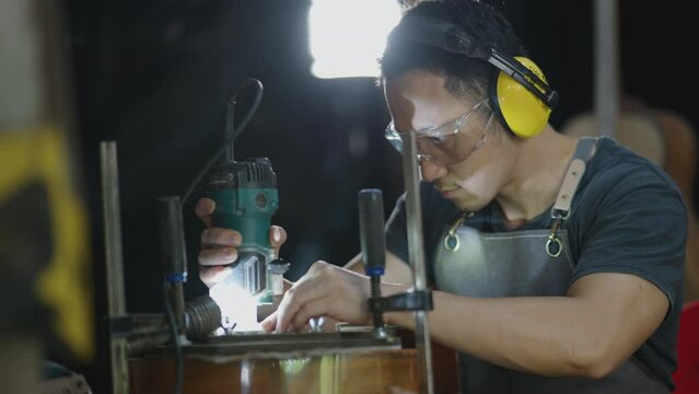 Guitar makers man wearing headphone to making acoustic guitars in laboratory. Asian guitar maker builds high quality guitars for musicians handmade guitar shop.Working fine woodusic, tradition guitar