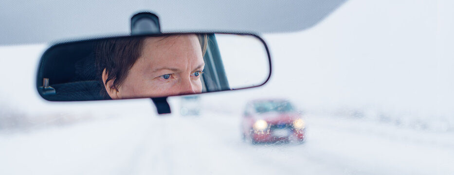 Face of a female driver in car rear-view mirror while driving in bad conditions during snow blizzard
