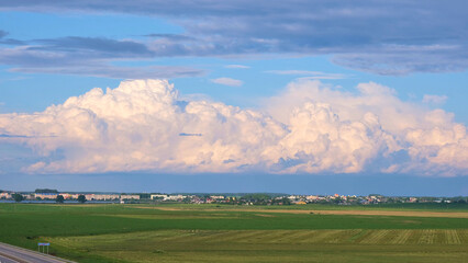 Fototapeta na wymiar Clouds over the green field near the road