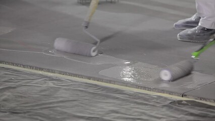 The builder works with a roller. Builders are making a polymer floor in the underground parking lot. Creation of an even high-strength floor