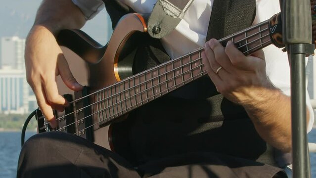 Close Up of Bass Player Hands Playing Rock Music with Bass Guitar at the Concert at the outdoor wedding party area with Beautiful seascape.
