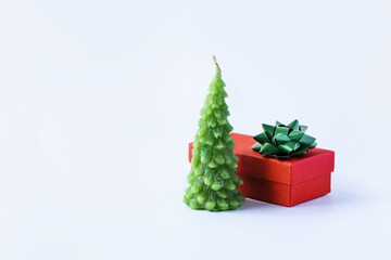 Christmas composition of a red gift box with a green bow and a green Christmas tree candle on a gray background with silver confetti stars