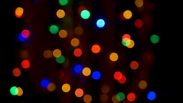 Multi-colored flashing lights of a garland in defocus on a black background