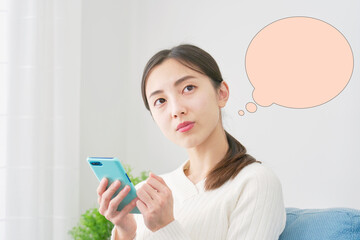 リビングでスマホを持って考える女性　吹き出しあり