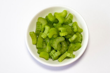 Cut fresh green celery in bowl on white table, flat lay.