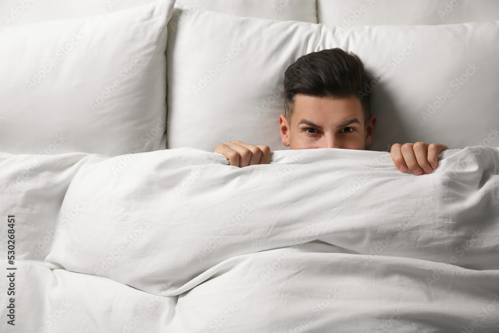 Wall mural Handsome man covering his face with blanket while lying in bed at home