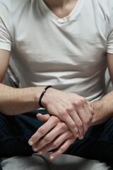Cropped close-up shot of man's hands with a black stone bracelet with a miniature hematite cross. The man is sitting and holding his hands with stone bracelet together. Front view.