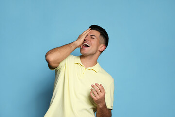Handsome man laughing on light blue background. Funny joke