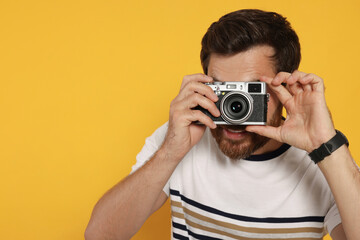 Man with camera taking photo on yellow background, space for text. Interesting hobby