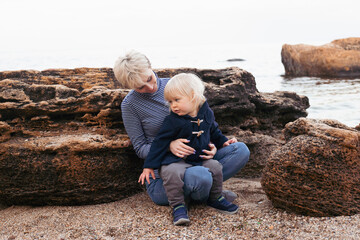 happy mother and son playing near sea on seashore in autumn time