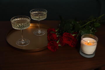 Burning candle, glasses of wine and beautiful red roses on wooden table indoors