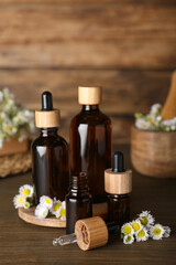Fototapeta na wymiar Bottles of chamomile essential oil and flowers on wooden table