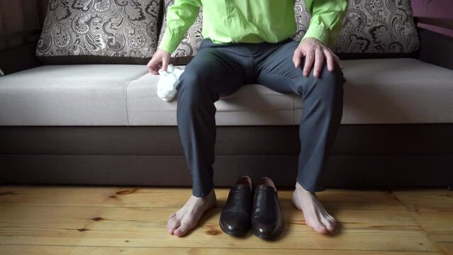 a man puts on socks on the couch,the man put on leather shoes, the businessman put on shoes