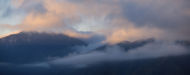 Fototapeta premium Dawn in the mountains, fog and clouds on the peaks, panoramic view