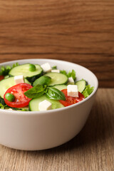 Tasty fresh salad with cucumber in bowl on wooden table, closeup