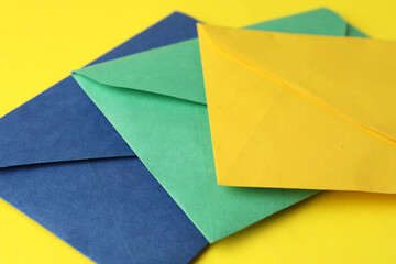 Colorful paper envelopes on yellow background, closeup