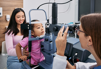 Cute little Asian girl getting eye exam at ophthalmology clinic with optometrist. Checking retina...