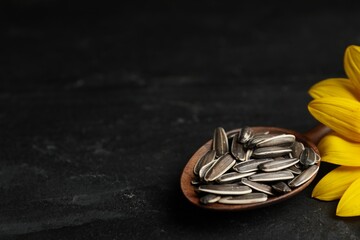 Raw sunflower seeds and flower on black table, closeup. Space for text
