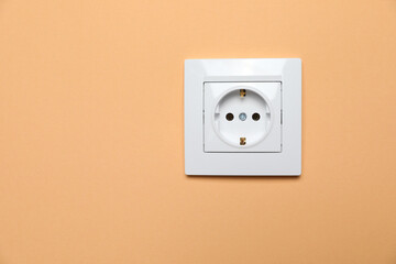 Power socket on pale orange wall, space for text. Electrical supply