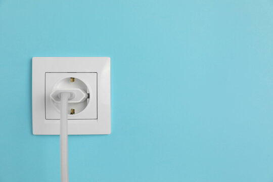 Charger adapter plugged into power socket on light blue wall, space for text. Electrical supply