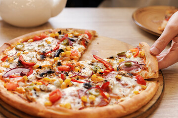 A woman's hand takes a piece of pizza. Selective focus.