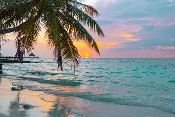 picturesque sunrise in the Maldives island, the sun rising from the Indian ocean and reflected in the water, travel concept, palm trees hanging over the water