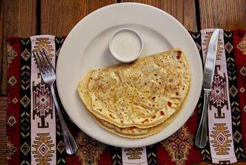 Yantyki with lamb fried in a dry frying pan and greased with butter with sour cream on a ceramic plate wnapkin, ith a napkin in the background. Upper layer. Crimean Tatar cuisine.