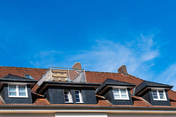 Fragment of a tiled roof with skylights and a small balcony. Blue sky with light clouds.