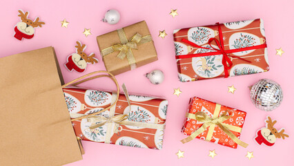 Fototapeta premium Christmas gifts with ribbons in eco friendly shopping bag on pastel pink background. Flat lay