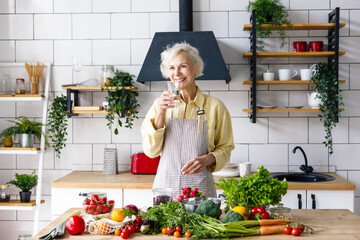beautiful elderly gray haired senior woman cook in cozy kitchen with fresh organic vegetables on...