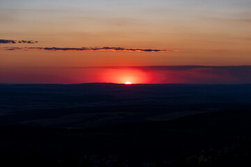 Landscape with sun, glowing sky and clouds. The sun is low, just before setting. View from Feldberg mountain in Hesse, Germany.