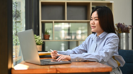 Fototapeta premium Asian woman office worker searching online information or typing business email on her laptop computer