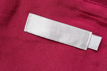 Blank white laundry care clothes label on red fabric texture background