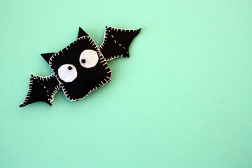 A black bat sewn from felt on a green background. A toy for Halloween.