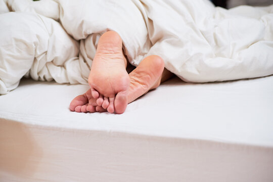 Close Up Of Feet Sticking Out Of A White Duvet In Bed