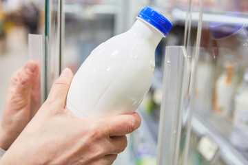 Hand hält eine Flasche mit veganer Milch am Kühlregal
