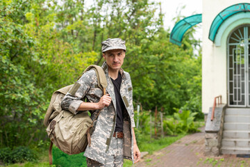 Photo of soldier in camouflaged uniform holding olive colored backpack
