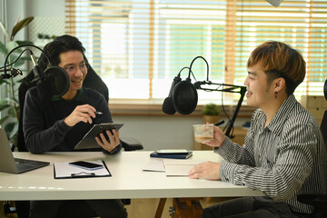 Two young podcaster using condenser microphone recording or streaming podcast from home studio