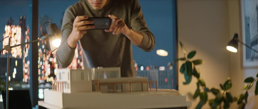 Portrait of Caucasian male architect or student working on a house project scale model late at home, using AR augmented reality application on his phone