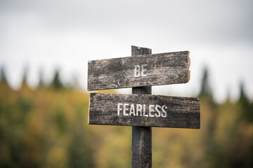 vintage and rustic wooden signpost with the weathered text quote be fearless, outdoors in nature. blurred out forest fall colors in the background.