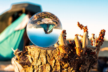 Glass lens globe outdoors at sunset on blue sky background with lots of ladybugs and camping tent...