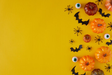 Creative holiday horror concept with bats, eyeballs, pumpkins and spiders on yellow background with copy space. Spooky idea. Halloween minimal concept.