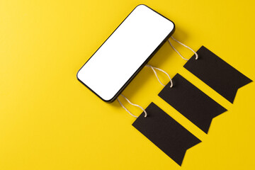 Composition of smartphone with gift tags on yellow background - Powered by Adobe